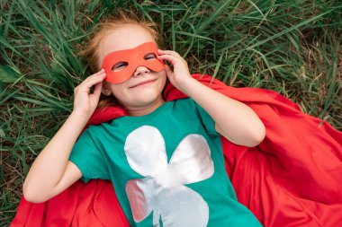 bir çocuk kırmızı süper kahraman pelerin ve yeşil çim üzerinde yalan maskesi havai görünümü