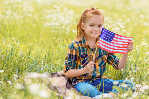 cute kid with american flagpole resting on green grass in field