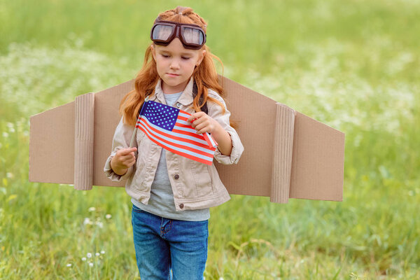 portrait of kid in pilot costume with american flagpole standing in meadow