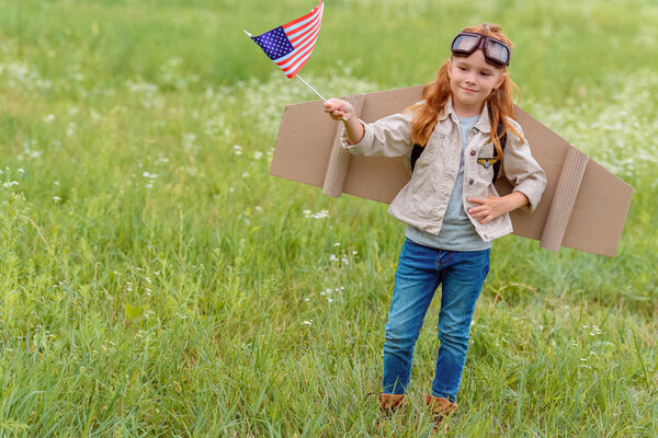 ребенок в костюме пилота с американским флагштоком, стоящим на лугу
