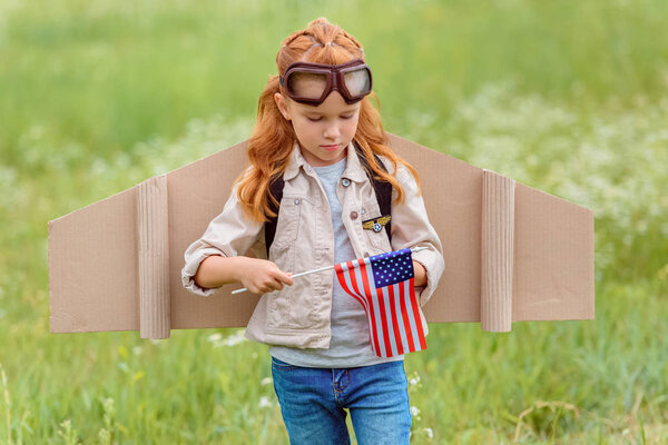 portrait of kid in pilot costume with american flagpole standing in meadow