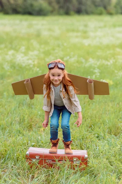 夏の畑でレトロなスーツケースからジャンプ パイロットの衣装で子供の笑顔 — ストック写真