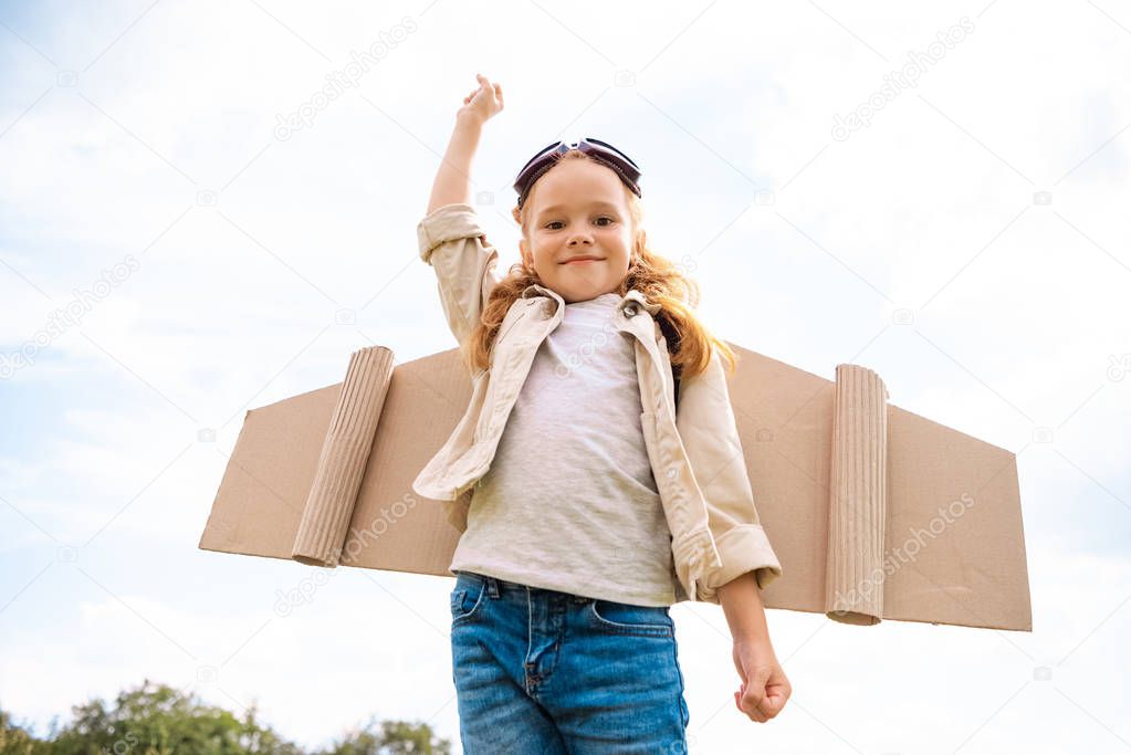low angle view of smiling child in pilot costume with hand up against blue cloudy sky