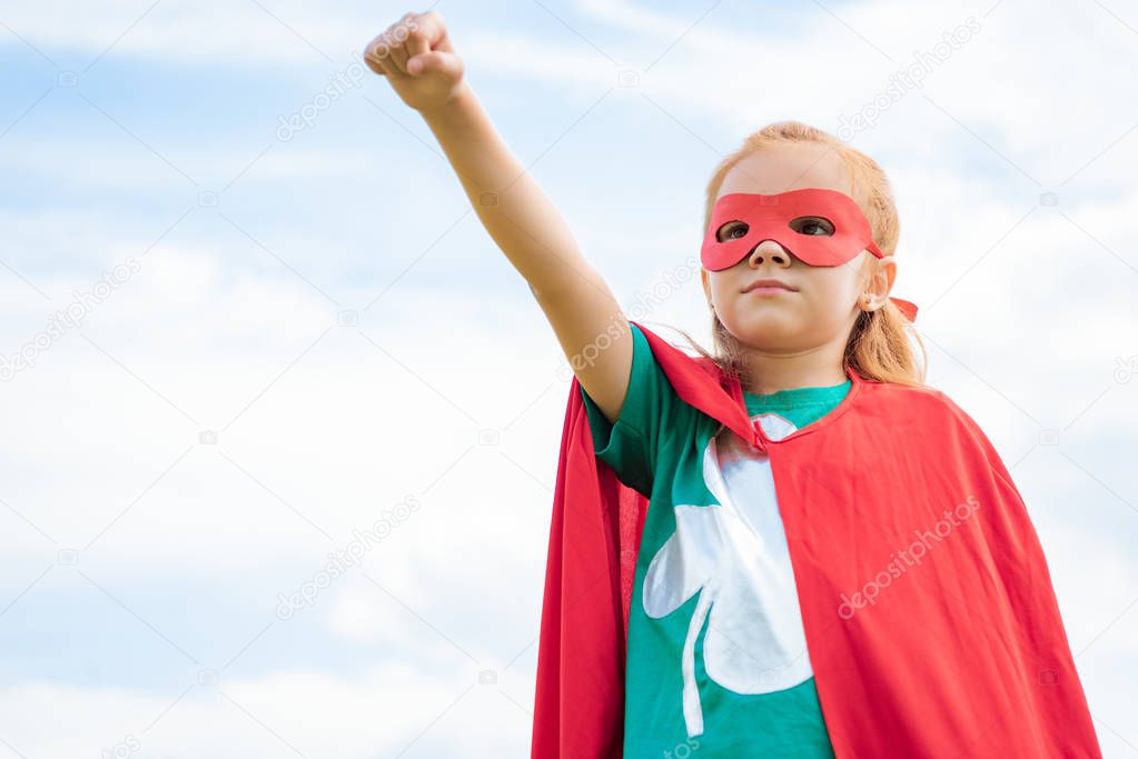 adorable child in superhero costume with outstretched arm and blue cloudy sky on background