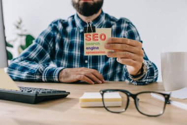 Seo - arama motoru optimizasyonu ile etiket tutan genç sakallı geliştirici kırpılmış atış