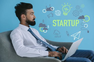 bearded businessman using laptop and sitting in armchair, on blue with startup icons and light bulb clipart