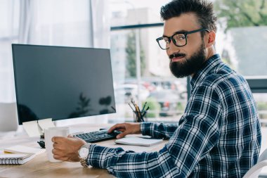 İşyerinde boş bilgisayar ekranı ile oturan ve kameraya bakarak Genç başarılı seo