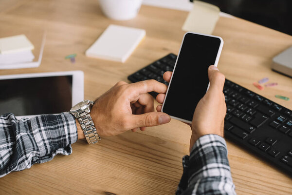 cropped shot of man using smartphone with blank screen at workplace
