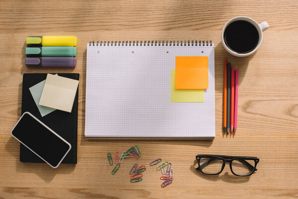 top view of office supplies, stick notes, smartphone, paper clips, notebook and cup of coffee
