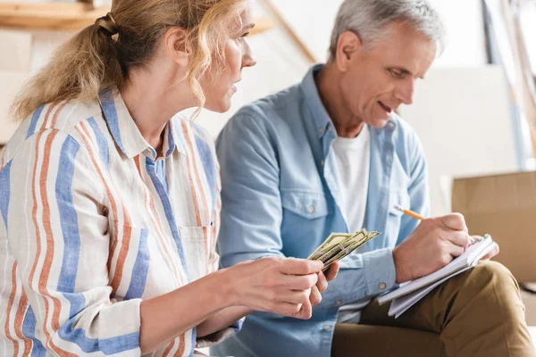 elderly couple counting money and taking notes in notebook during relocation