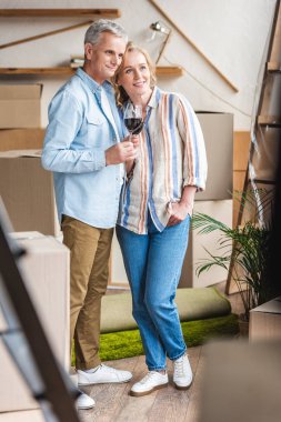 happy senior couple holding glasses of wine and looking away while moving home   clipart