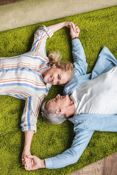 在搬迁期间躺在地毯上和牵手的幸福的老夫妇的最高视图 — 图库照片