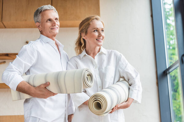 happy senior couple holding yoga mats and looking away