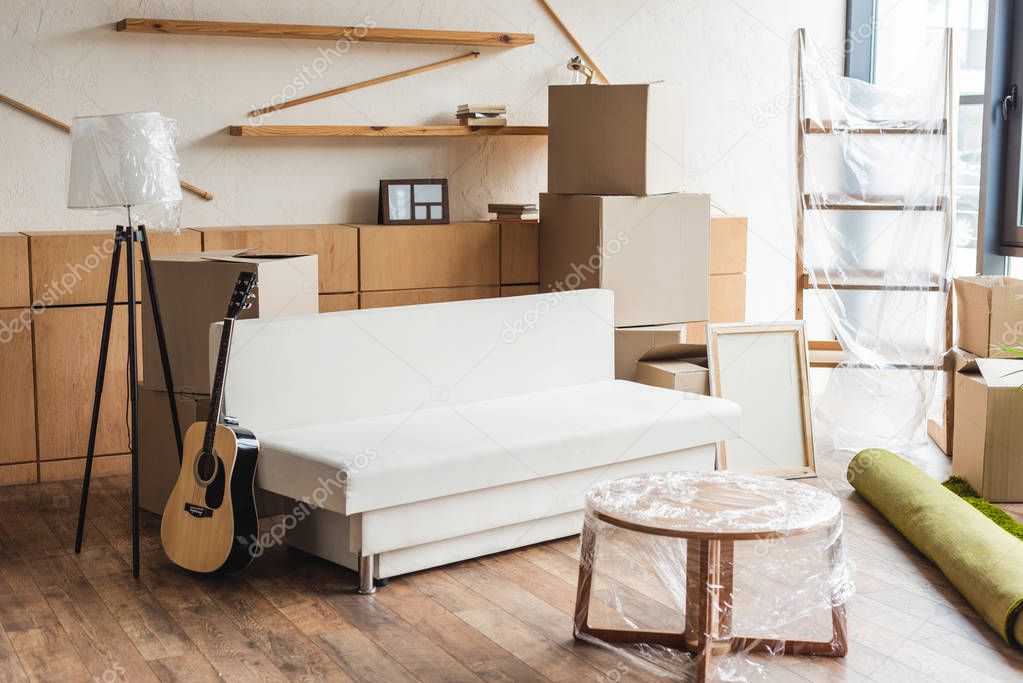 cardboard boxes, rolled carpet, guitar and furniture in new apartment during relocation