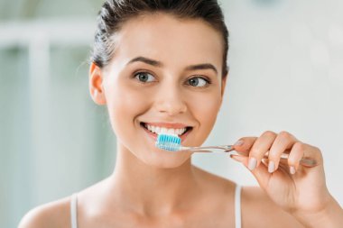 beautiful smiling girl brushing teeth in bathroom clipart
