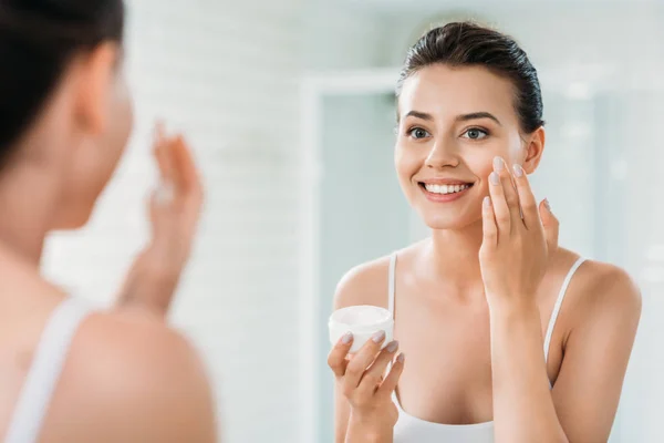Bela Menina Feliz Aplicando Creme Facial Olhando Para Espelho Banheiro — Fotografia de Stock