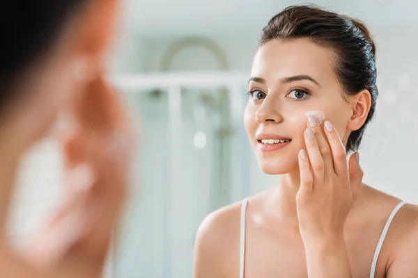 Enfoque Selectivo Joven Sonriente Aplicación Crema Facial Mirando Espejo Baño — Foto de Stock