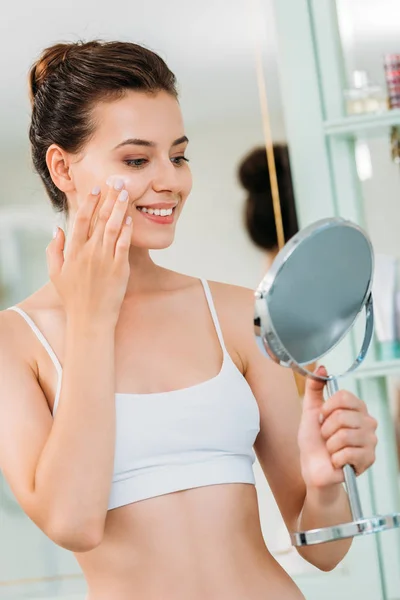 Smiling Young Woman Holding Mirror Applying Facial Cream Bathroom — Stock Photo, Image