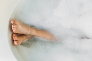 partial view of beautiful female legs in bathtub with foam clipart