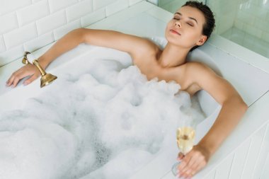 güzel genç kadının kapalı gözler kadeh şampanya ve köpüklü banyo küvetinde rahatlatıcı holding ile yüksek açılı görünüş