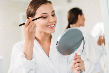 beautiful smiling brunette girl applying makeup in bathroom clipart