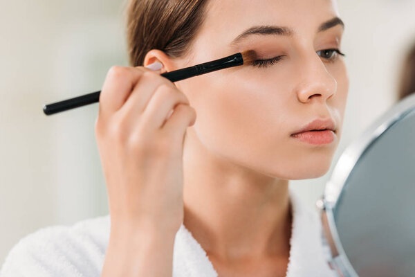 close-up view of beautiful young woman applying eyeshadow with brush 