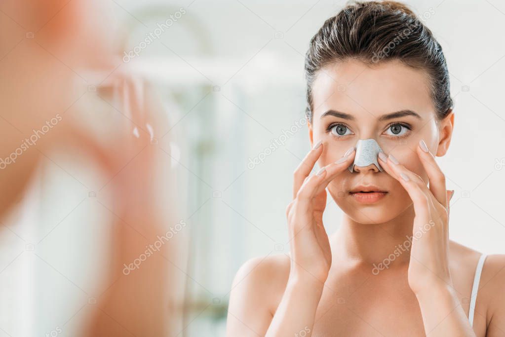 attractive girl applying nose strip and looking at mirror on bathroom  