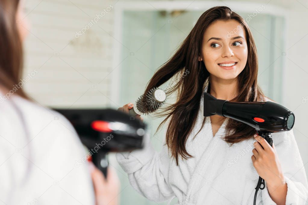 happy young woman drying hair at mirror in bathroom 