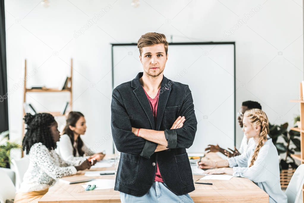portrait of young businessman with arms crossed standing at table during conference in office 