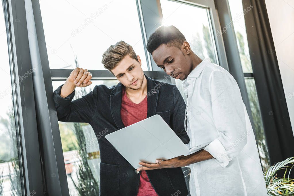 multicultural confident businessmen working on laptop together in office