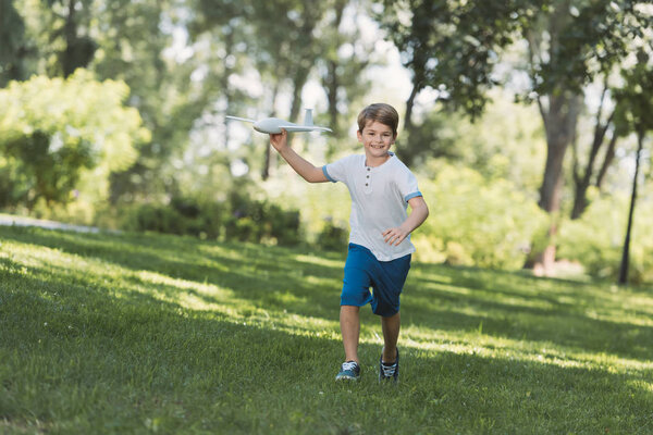 adorable happy boy holding toy plane and smiling at camera in park