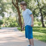 Netter glücklicher Junge fährt Skateboard und lächelt in die Kamera im Park