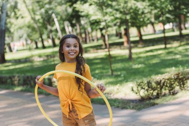 cute happy child holding hula hoop and smiling at camera in park  clipart
