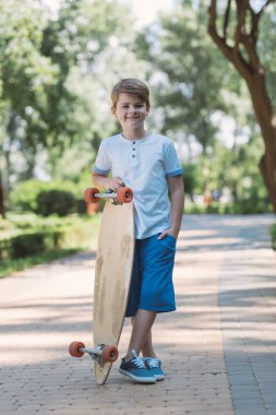 Longboard ile ayakta ve kamera Park gülümseyen şirin mutlu çocuk  