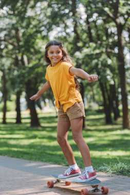 beautiful smiling child riding longboard in park clipart