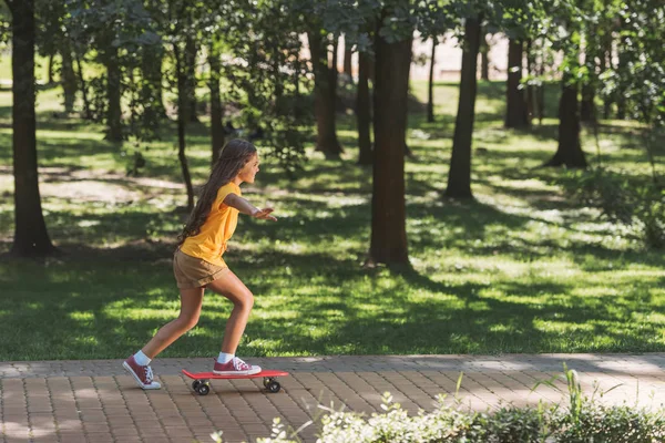 公園でスケート ボードに乗ってかわいらしい子供の側面図 — ストック写真