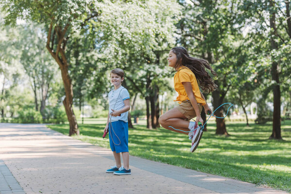 adorable happy kids playing and jumping with skipping ropes in park 