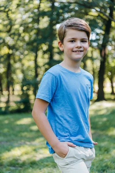 ポケットの手で立っている 公園にカメラで笑顔の愛らしい子供の肖像画 — ストック写真