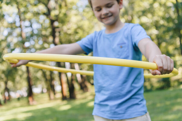 cropped shot of adorable happy child playing with hula hoop in park