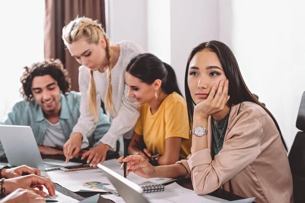 Tankefull Asiatisk Forretningskvinne Som Sitter Ved Bordet Mens Kollegene Diskuterer – stockfoto