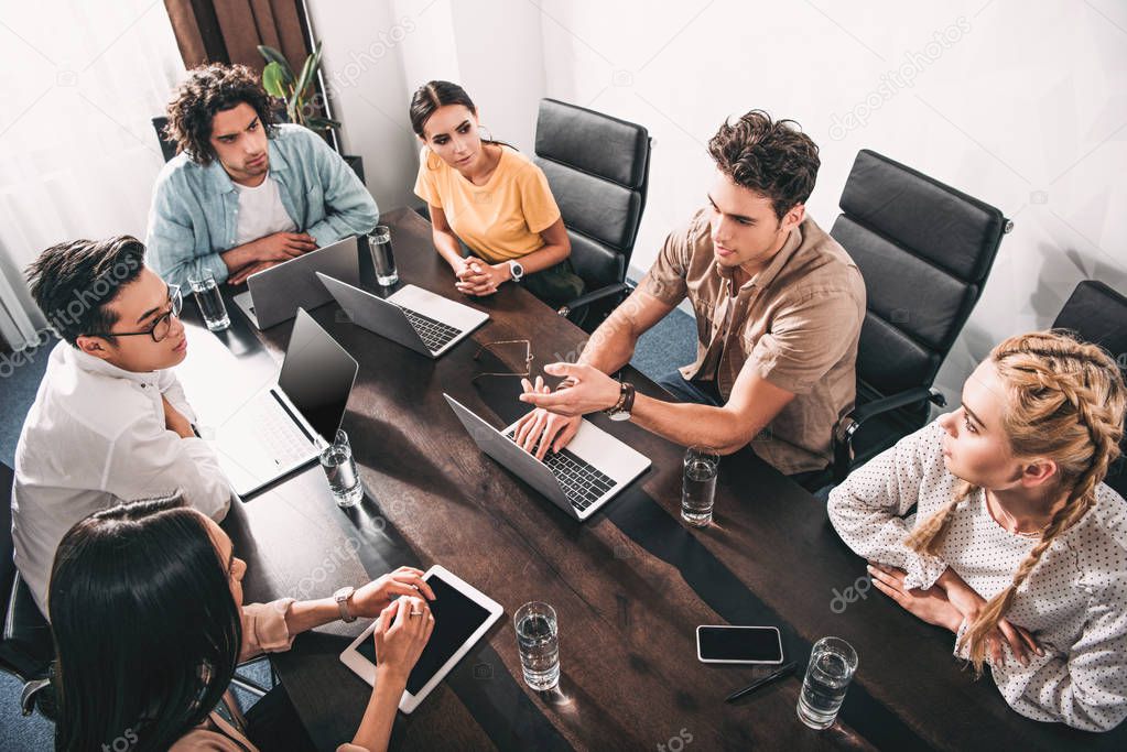 high angle view of multicultural business partners having meeting at table with laptops in modern office 