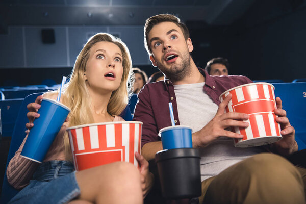 emotional couple with popcorn watching film together in cinema