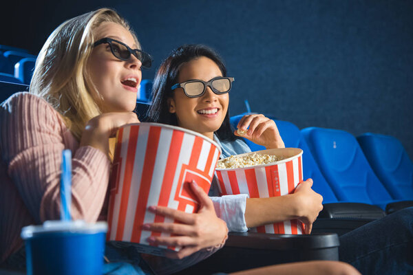 emotional multiracial women in 3d glasses with popcorn watching film together in movie theater