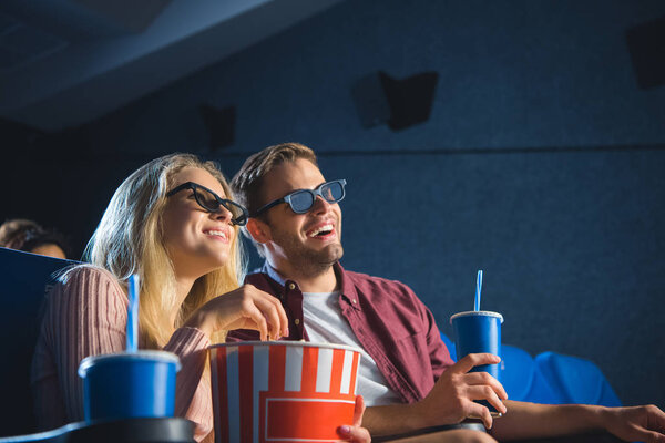 веселая пара в 3D-очках с попкорном, смотрящая фильм вместе в кино
