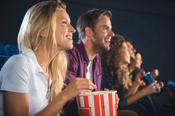 cheerful friends with popcorn watching film together in movie theater
