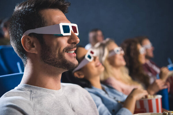 selective focus of multiethnic friends in 3d glasses with popcorn watching film together in movie theater