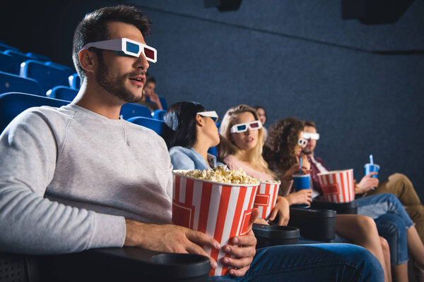 selective focus of multiethnic friends in 3d glasses with popcorn watching film together in movie theater