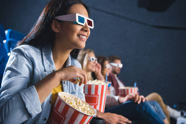 smiling asian woman in 3d glasses with popcorn watching movie in cinema