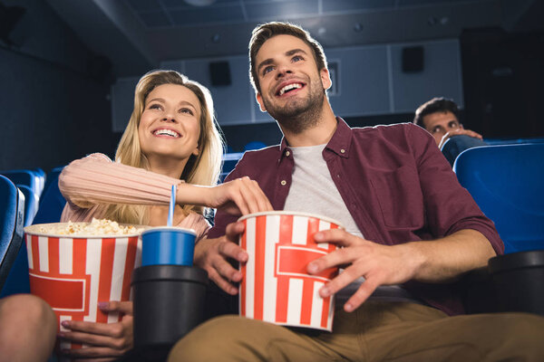 happy couple with popcorn and soda drink watching film together in cinema