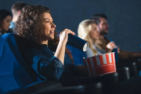 side view of woman with soda drink and popcorn watching movie in cinema